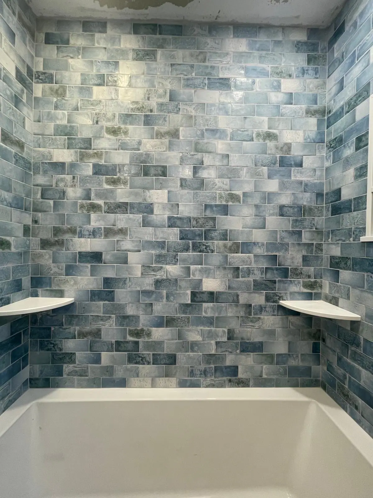 Front view of a tub surround in blue variegated subway tile with corner shelves