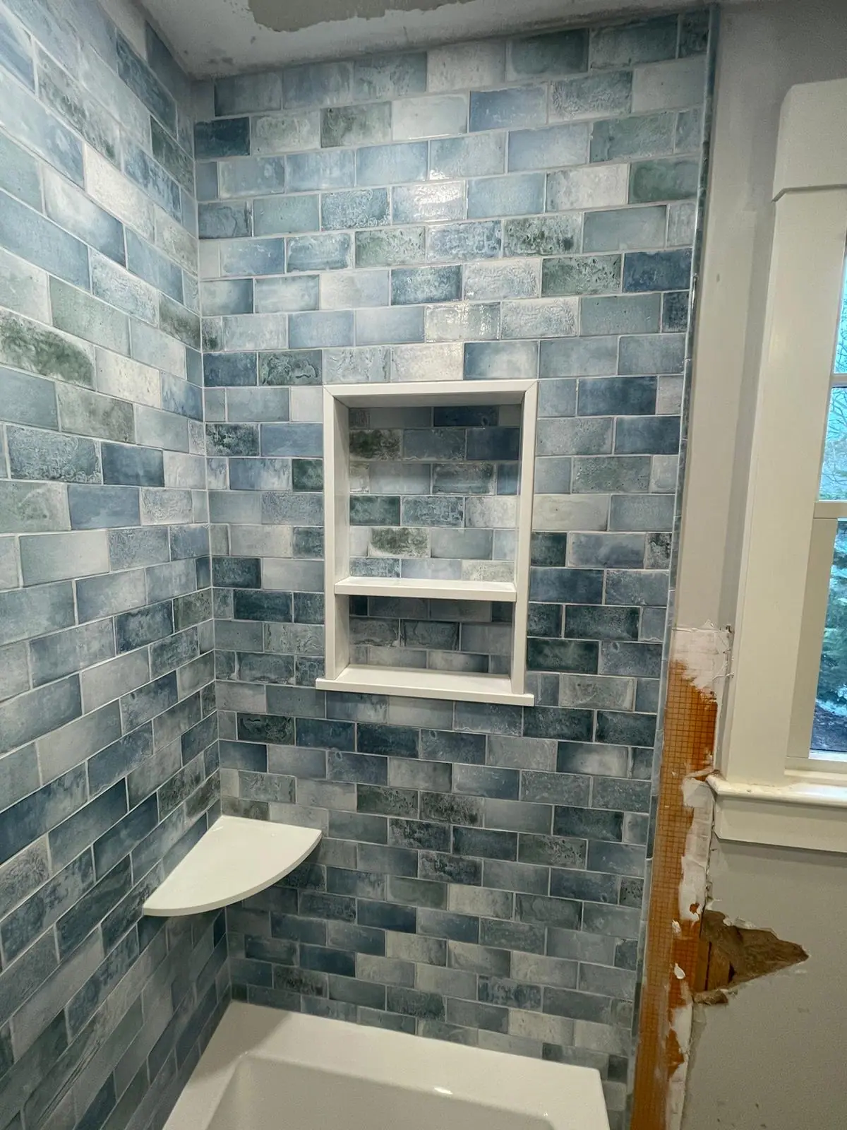 Two-shelf recessed niche framed in white within blue variegated subway tile