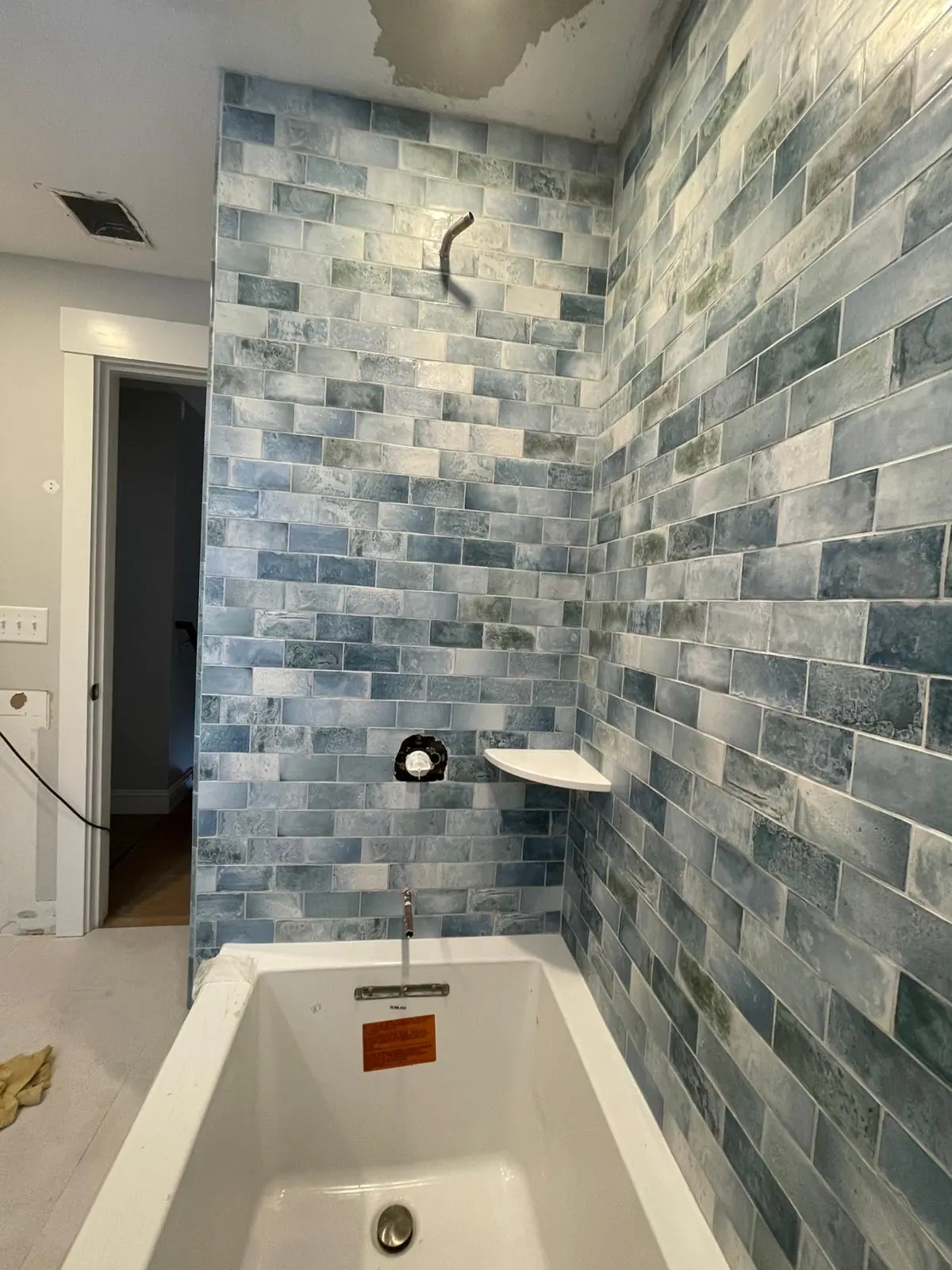 Tub surround in blue variegated subway tile with a corner shelf
