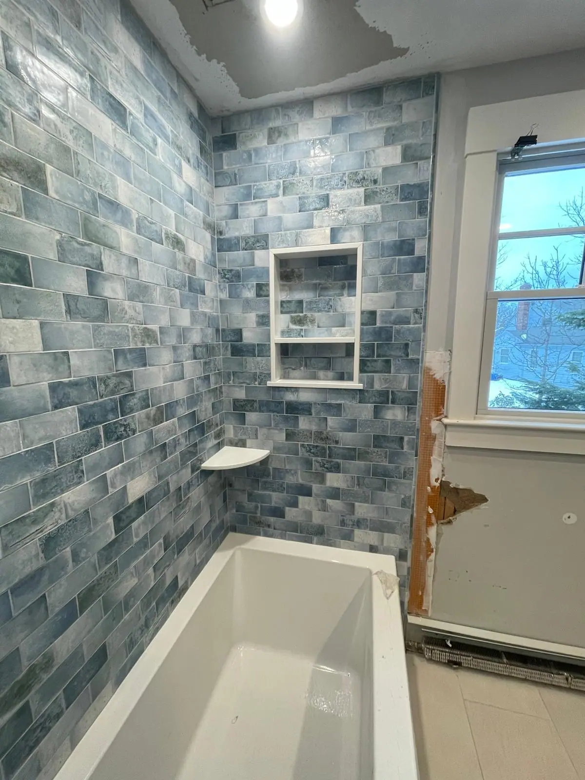 Tub surround in blue variegated subway tile with a two-shelf niche beside a window