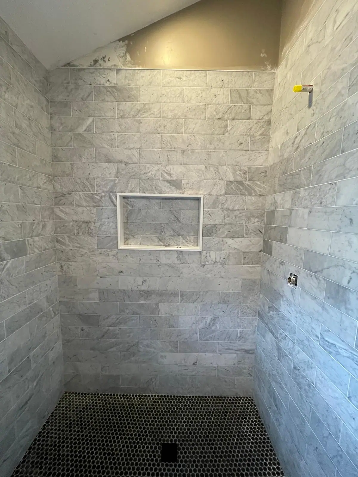Shower with gray veined subway tile, a framed niche and a black hexagon mosaic floor