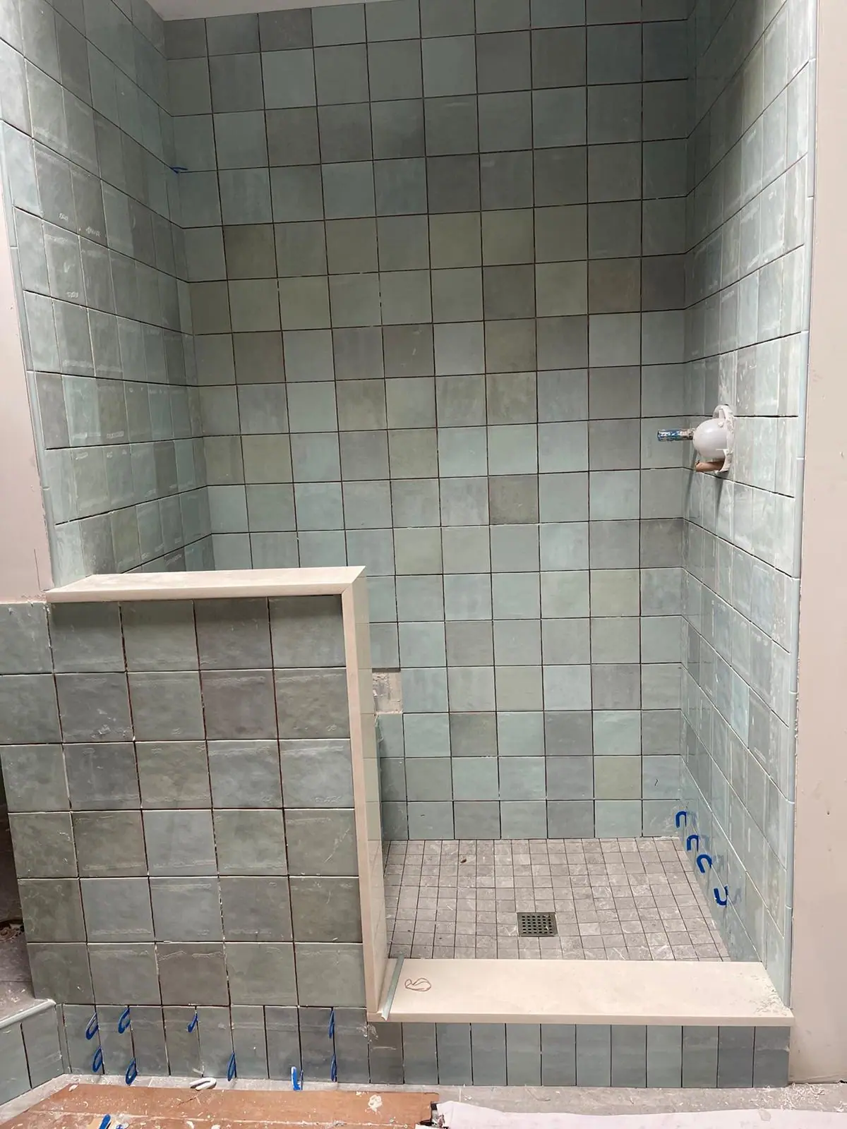 Walk-in shower in pale green square tile with a tiled bench and a mosaic floor
