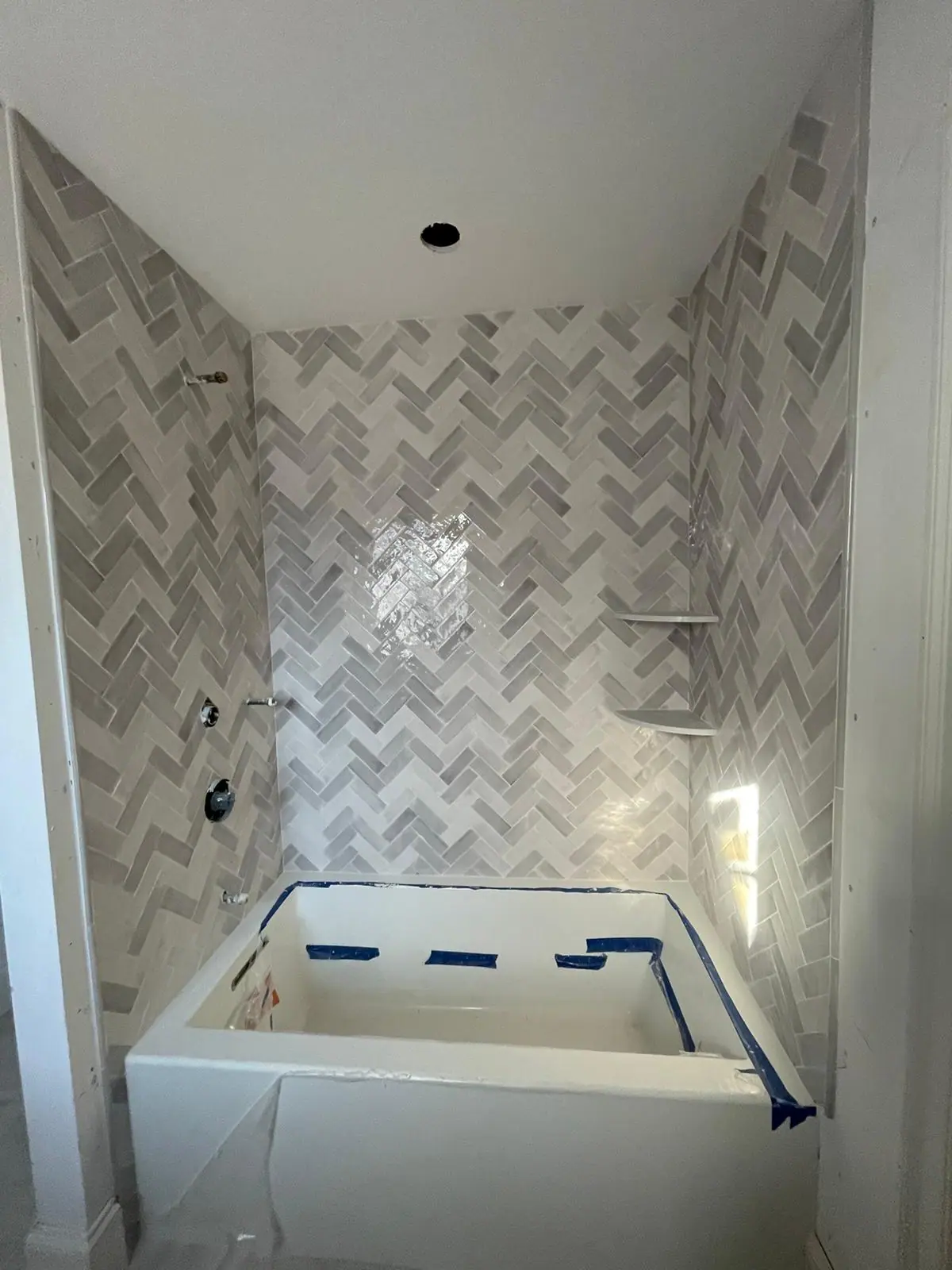 Tub surround in gray herringbone tile with corner shelves