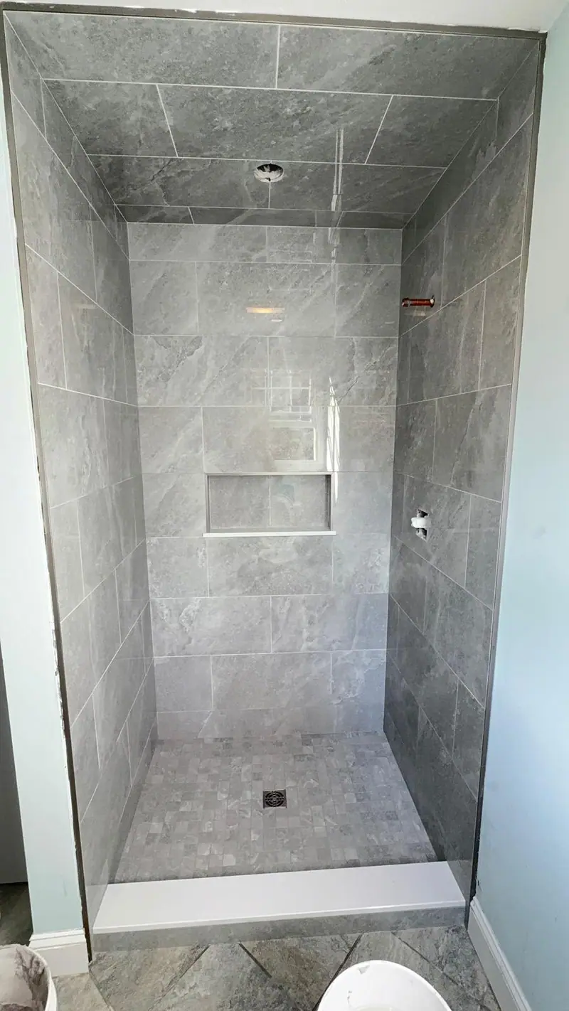 Shower with large-format gray tile on the walls and ceiling, a recessed niche and a mosaic floor