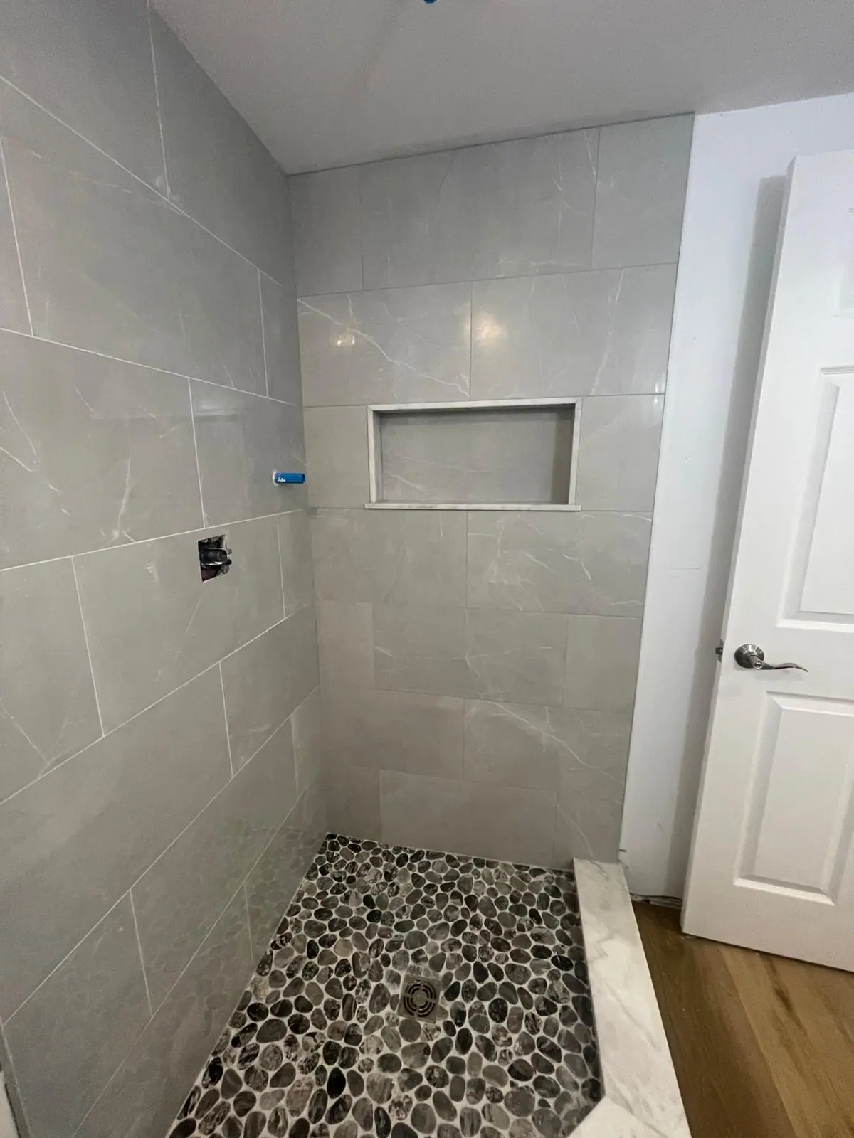 Shower with large-format light gray wall tile, a recessed niche and a dark pebble tile floor