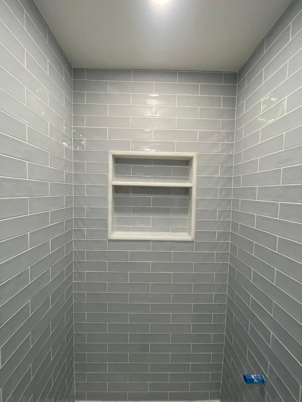 Light blue glossy subway tile with a two-shelf recessed niche
