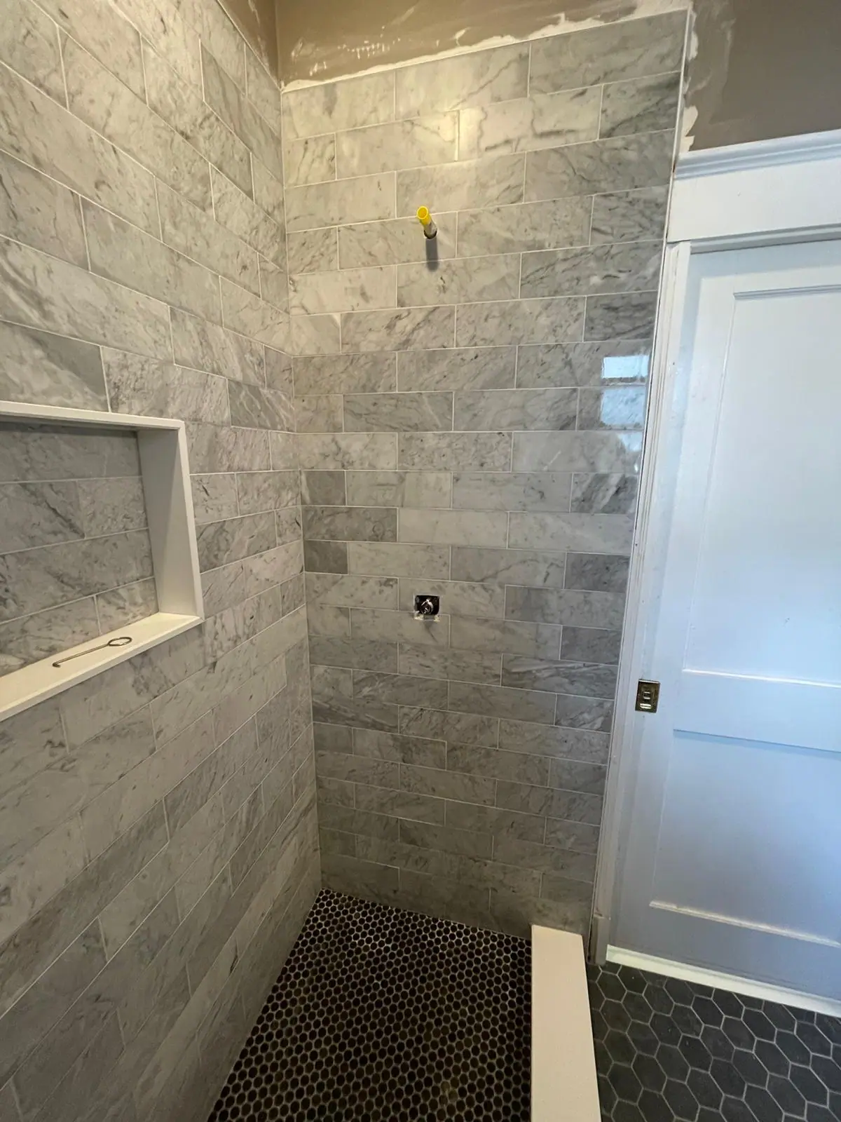 Shower with gray marble-look tile, a framed niche and a black hexagon mosaic floor