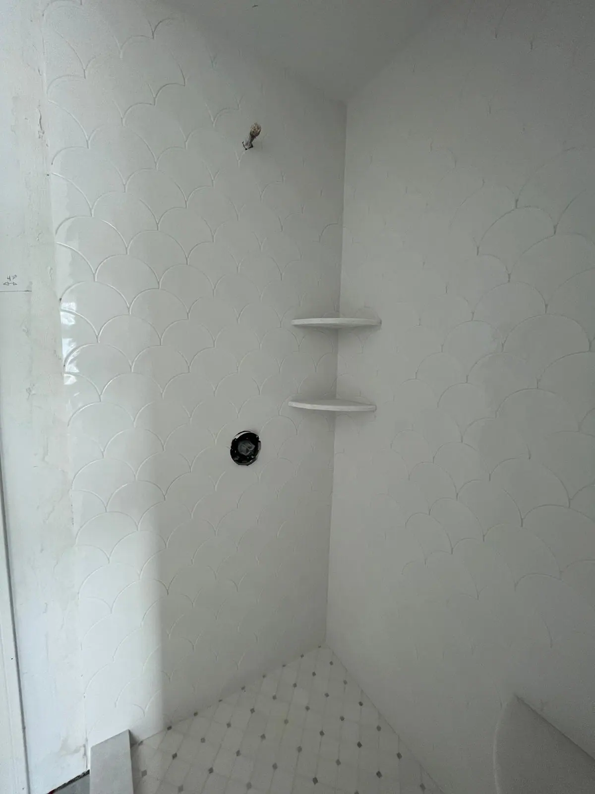 Shower with white marble-look wall tile, corner shelves and a dot mosaic floor