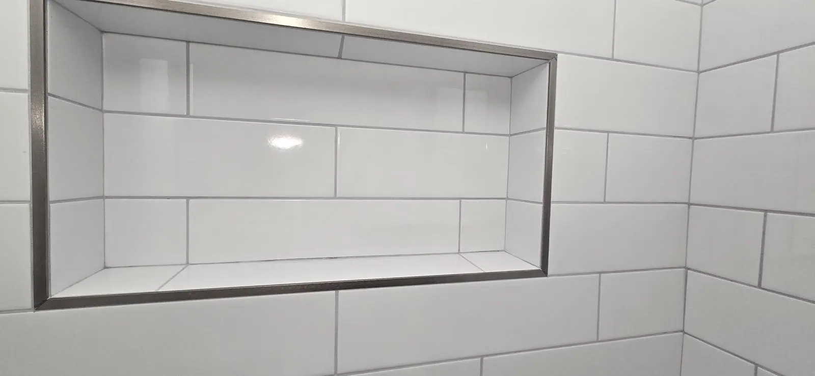 Close-up of a long recessed niche in white tile finished with a metal edge trim