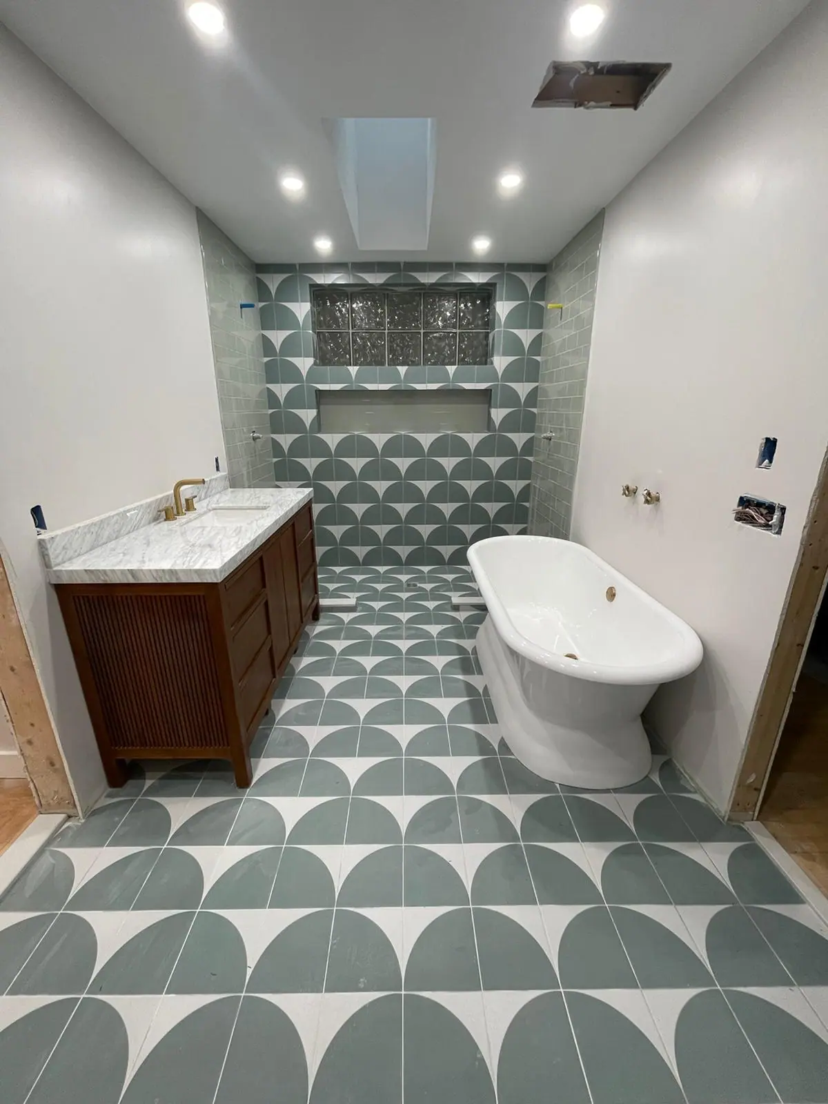 Finished bathroom with green and white patterned floor tile, a freestanding tub and a wood vanity