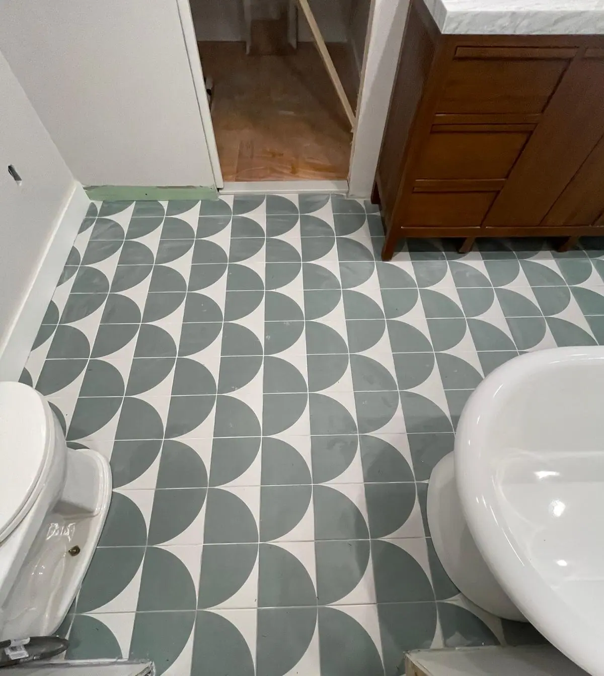 Green and white patterned floor tile around a pedestal sink and toilet