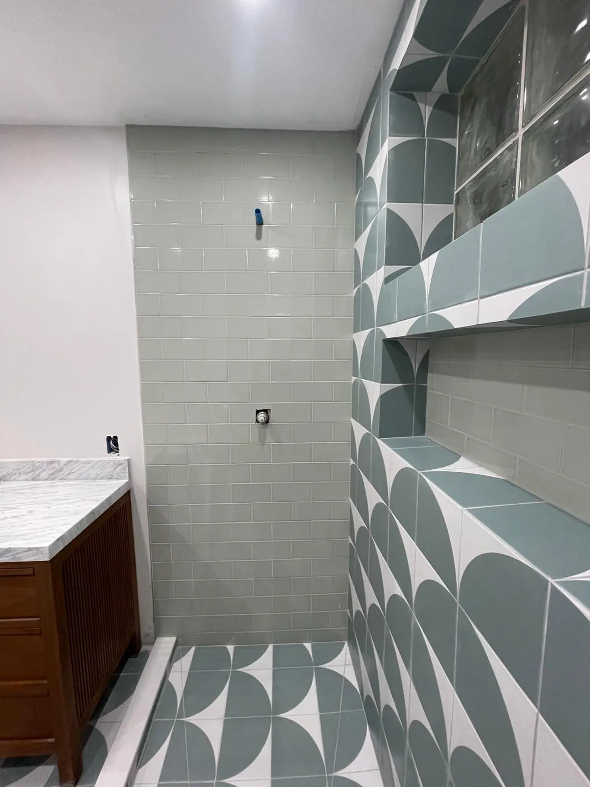 Shower wall with a long recessed niche in green and white patterned tile beside sage subway tile