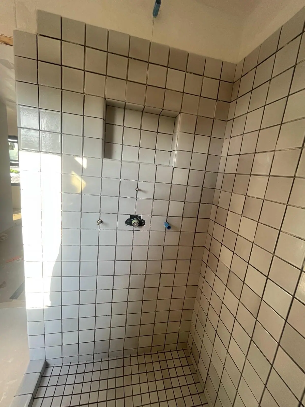 Shower in white square tile with contrasting dark grout and a recessed niche