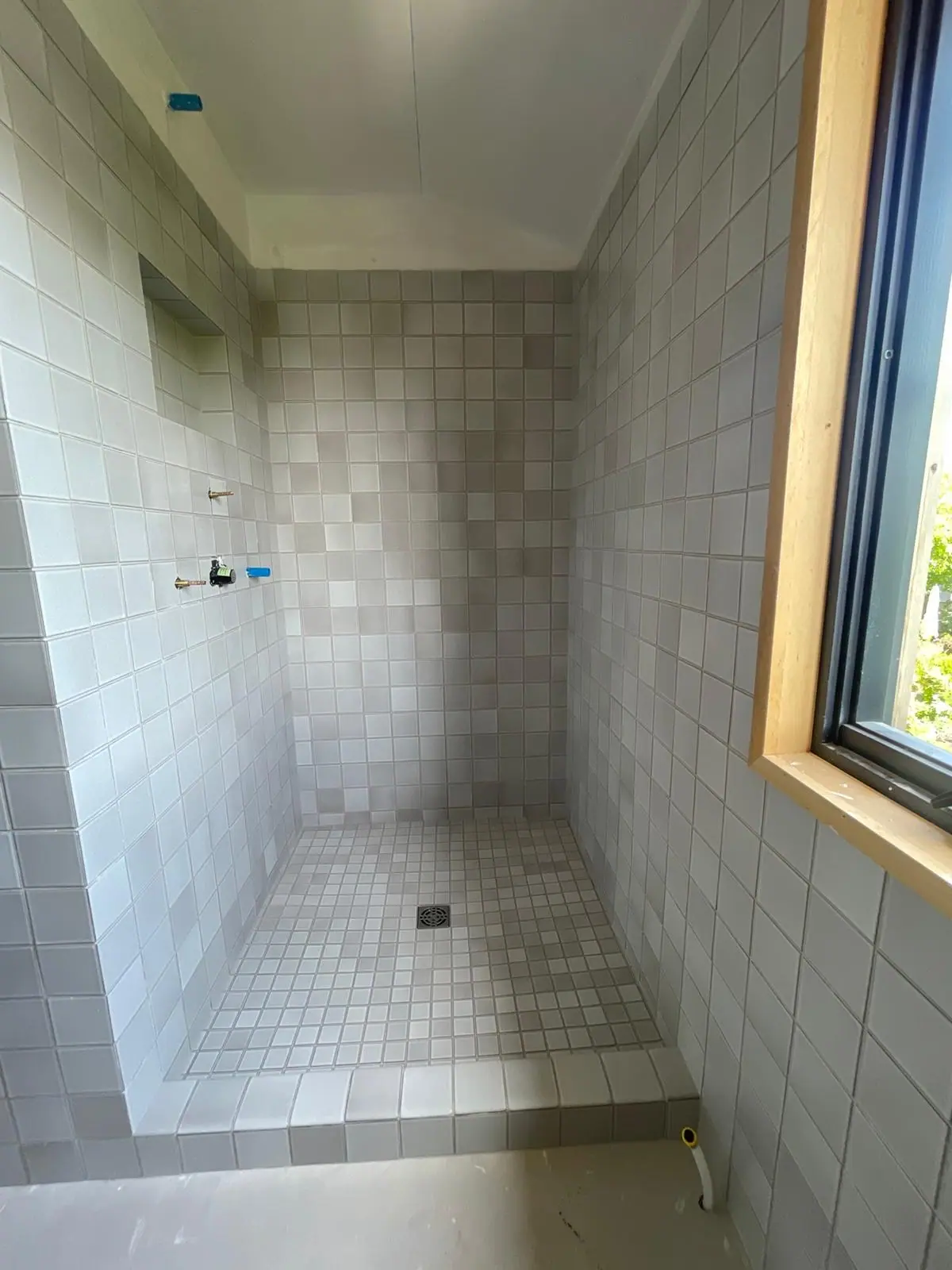 Shower in light gray square tile beside a window, with a mosaic floor