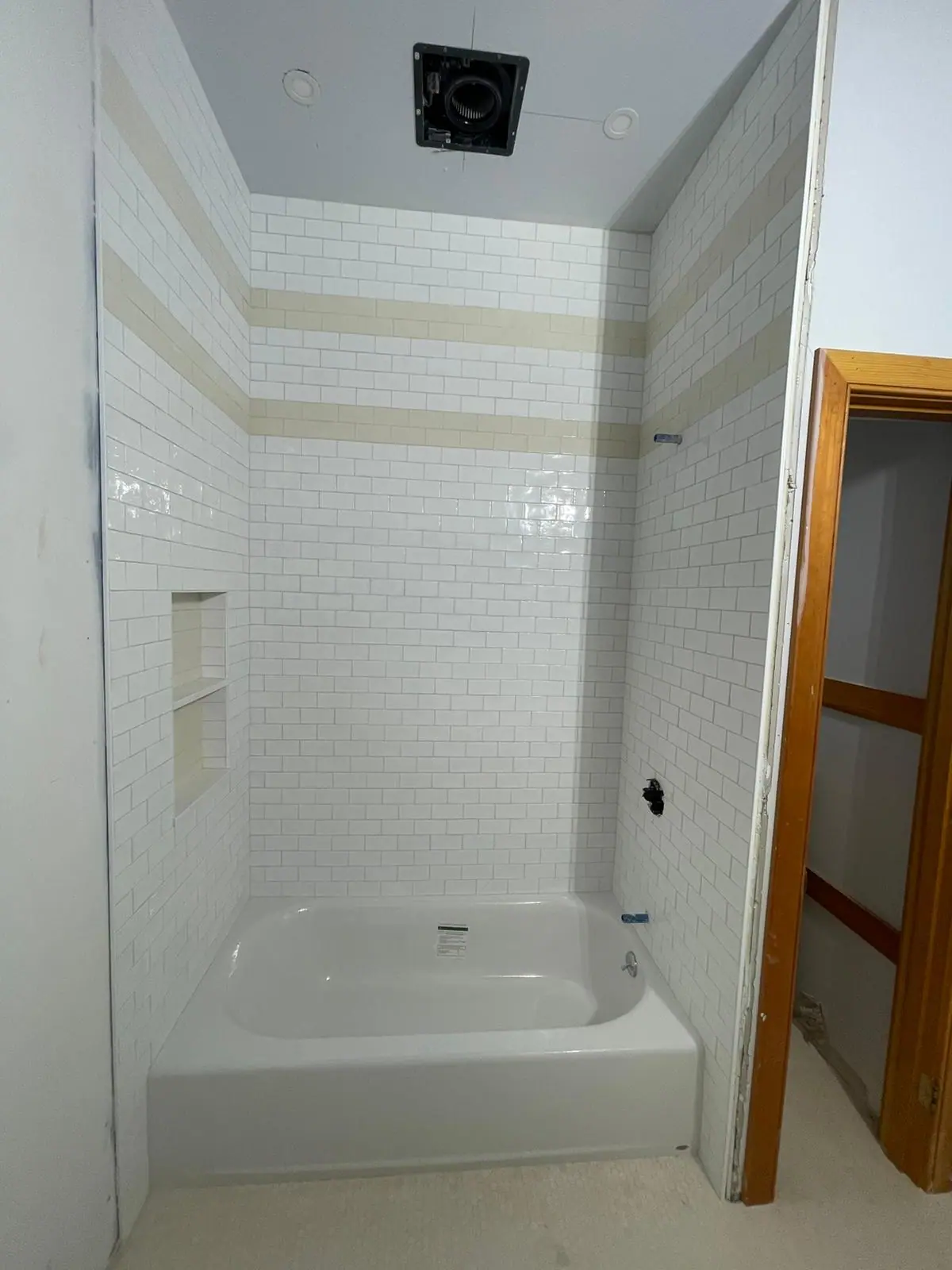 White subway tile tub surround with a beige accent band and a recessed niche