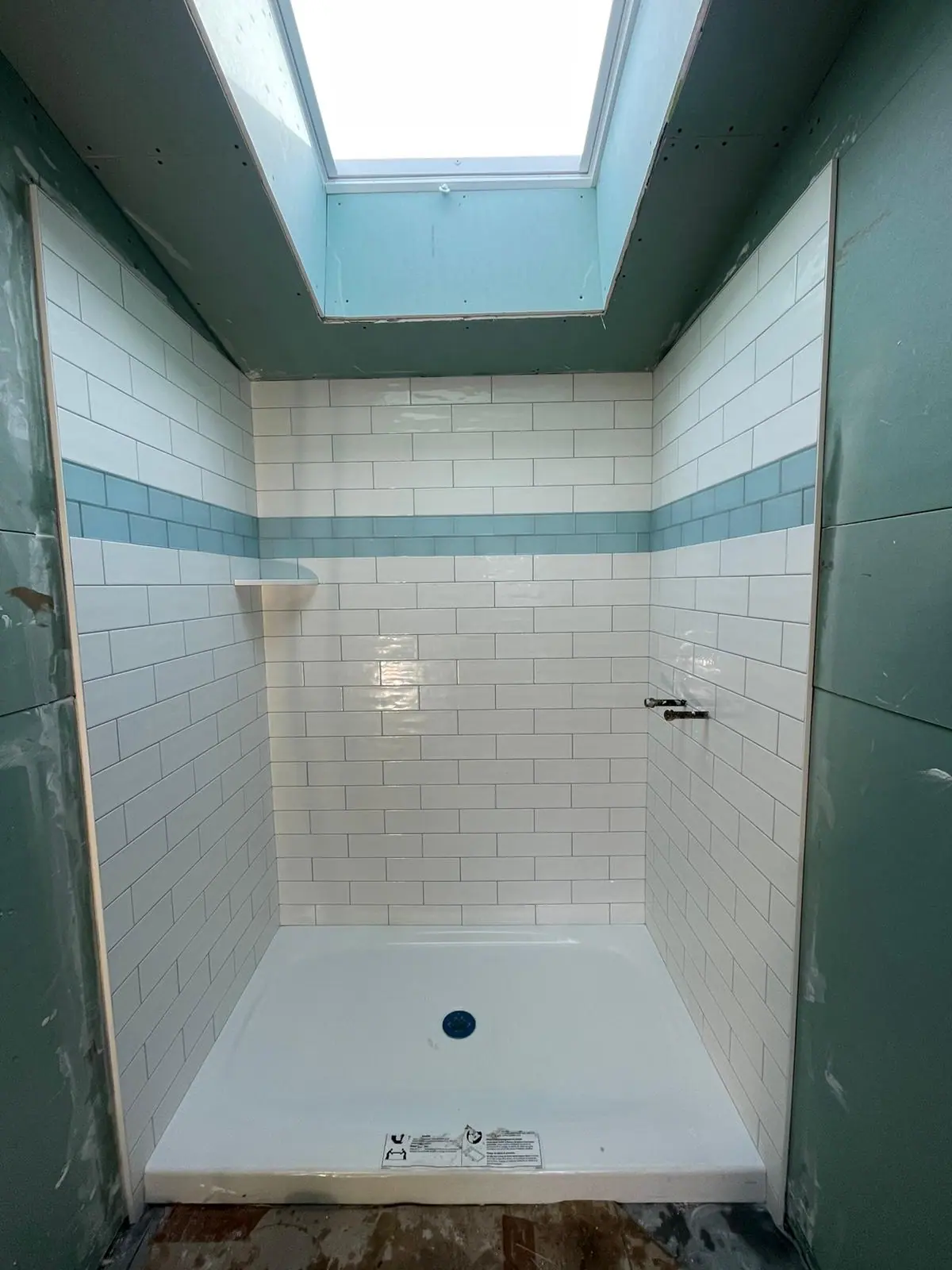 White subway tile shower with a blue glass accent stripe under a skylight