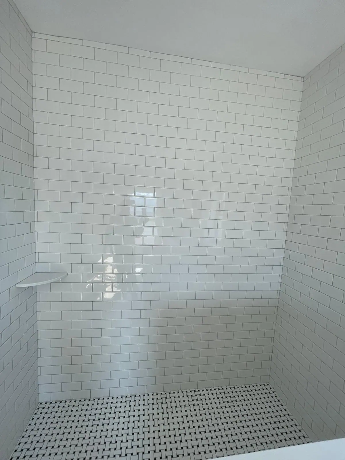 White subway tile shower walls with a corner shelf and a basketweave mosaic floor