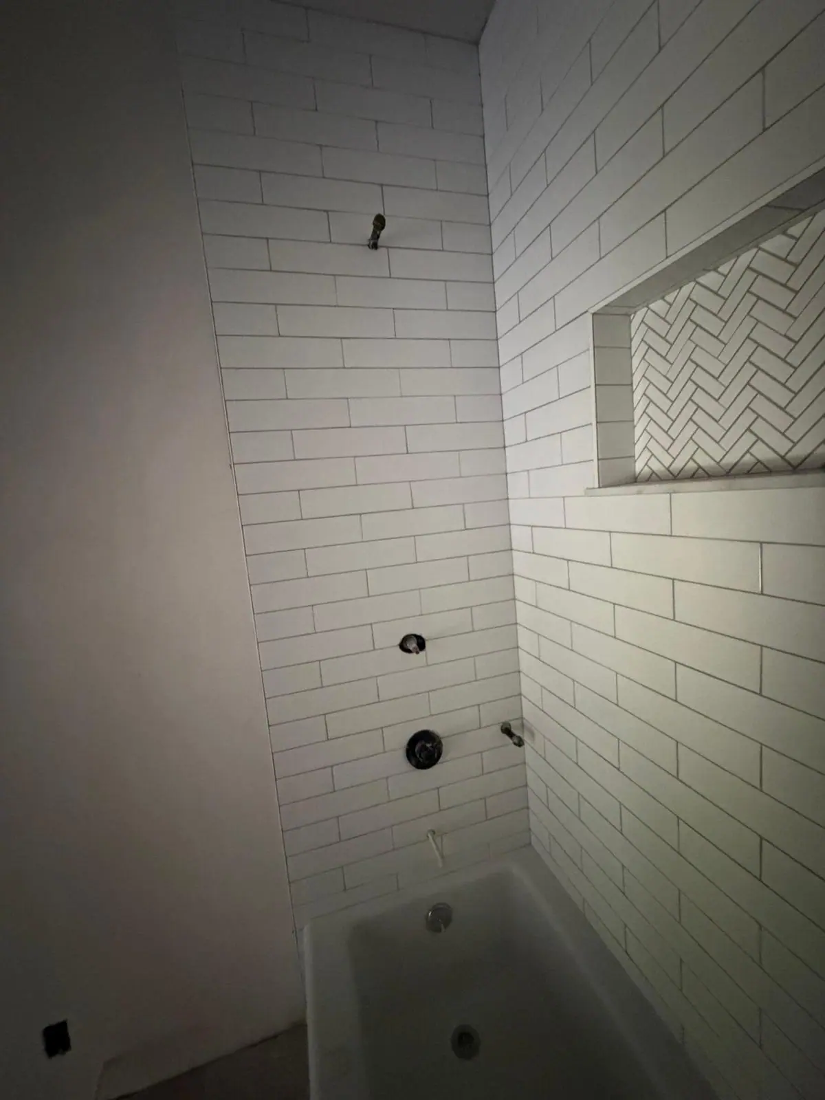 White subway tile tub surround with a long recessed niche lined in herringbone tile