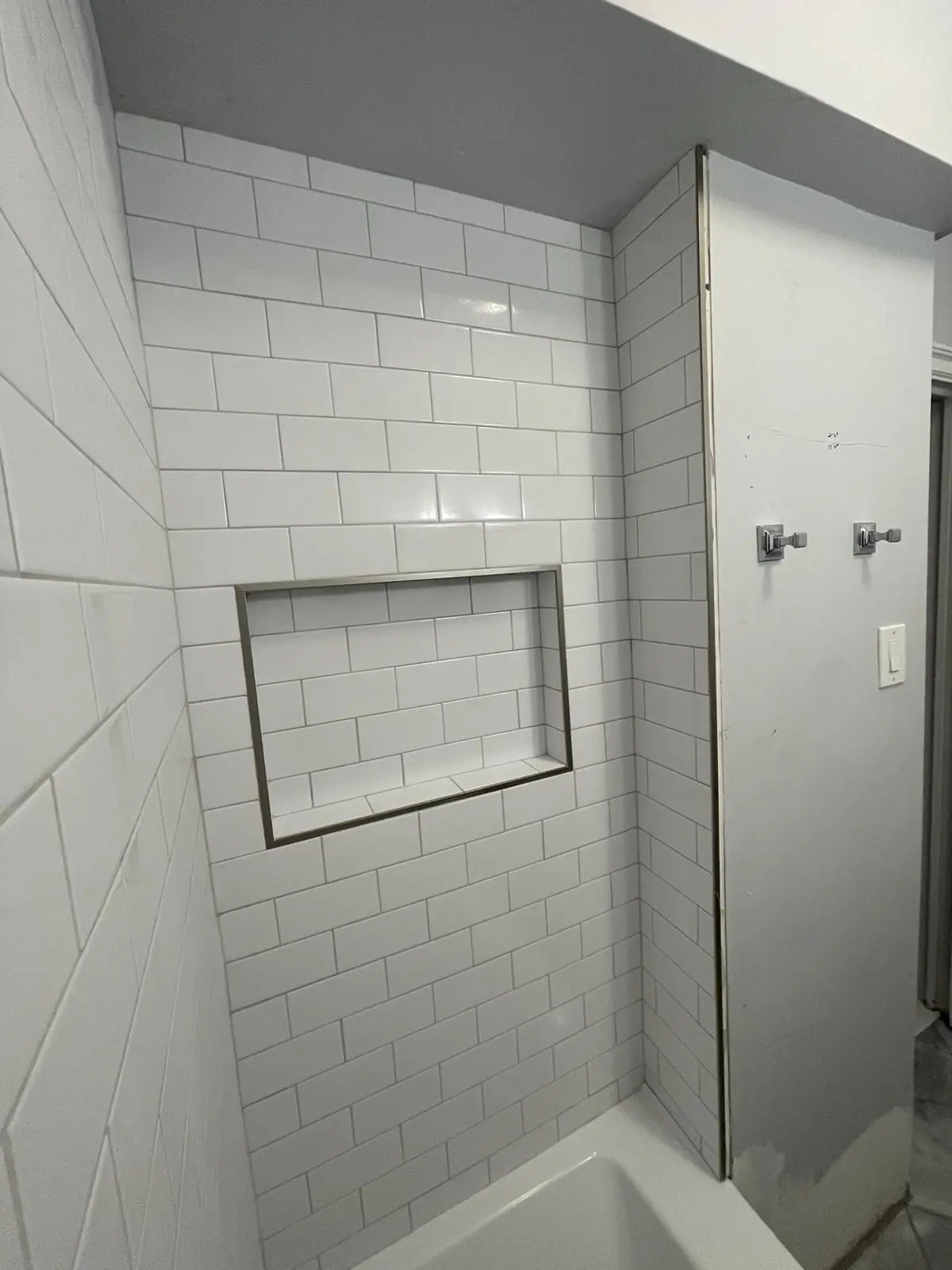 White subway tile tub surround with a recessed niche finished in dark metal trim
