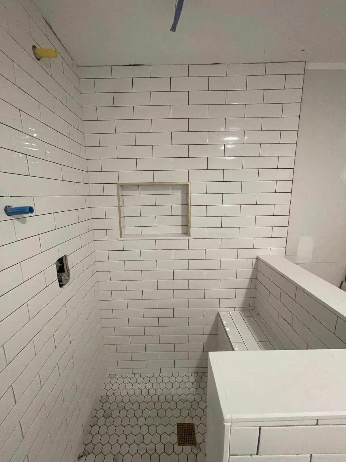 White subway tile shower with a recessed niche, a tiled half wall and a white hexagon floor