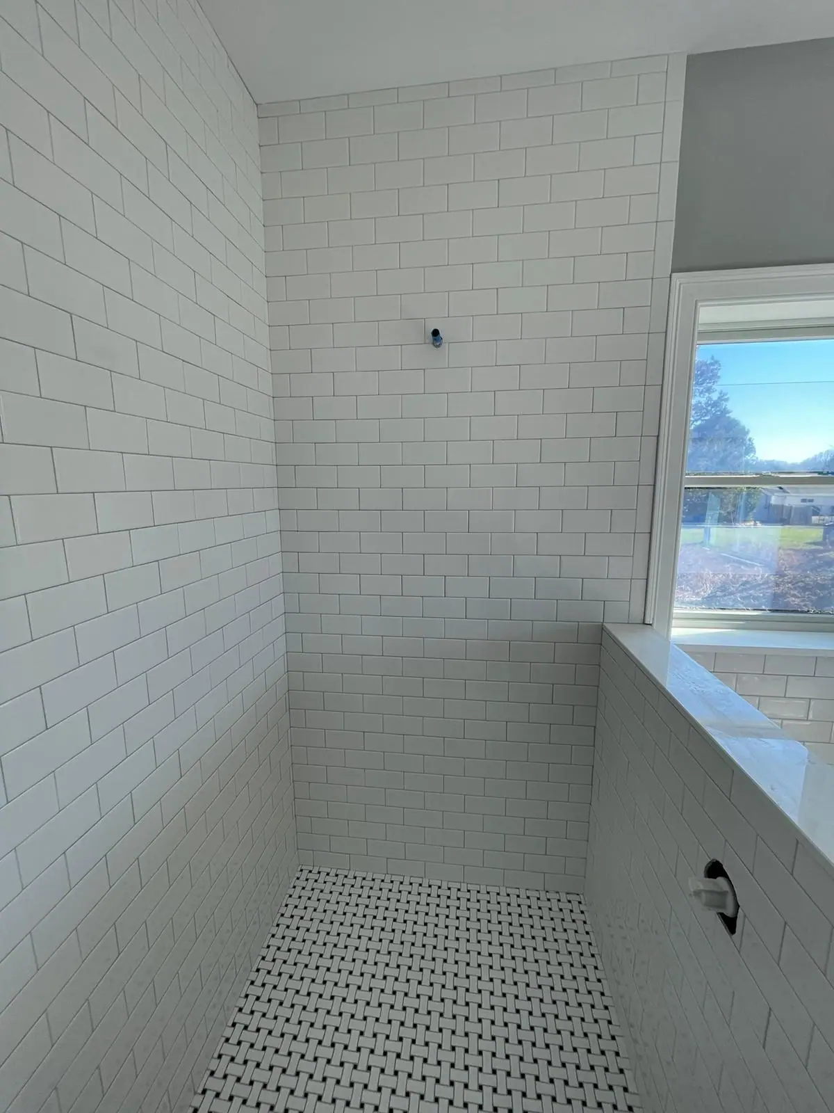 White subway tile shower with a tiled knee wall, a window and a basketweave mosaic floor