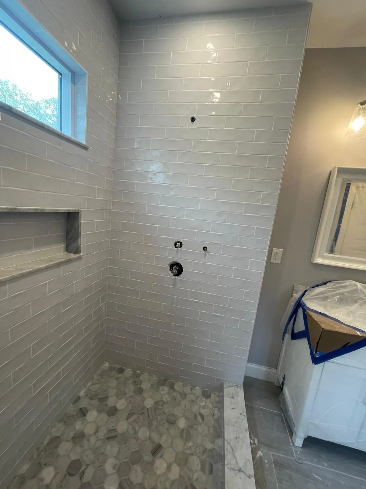 White subway tile shower with a window, a long recessed niche and a pebble mosaic floor