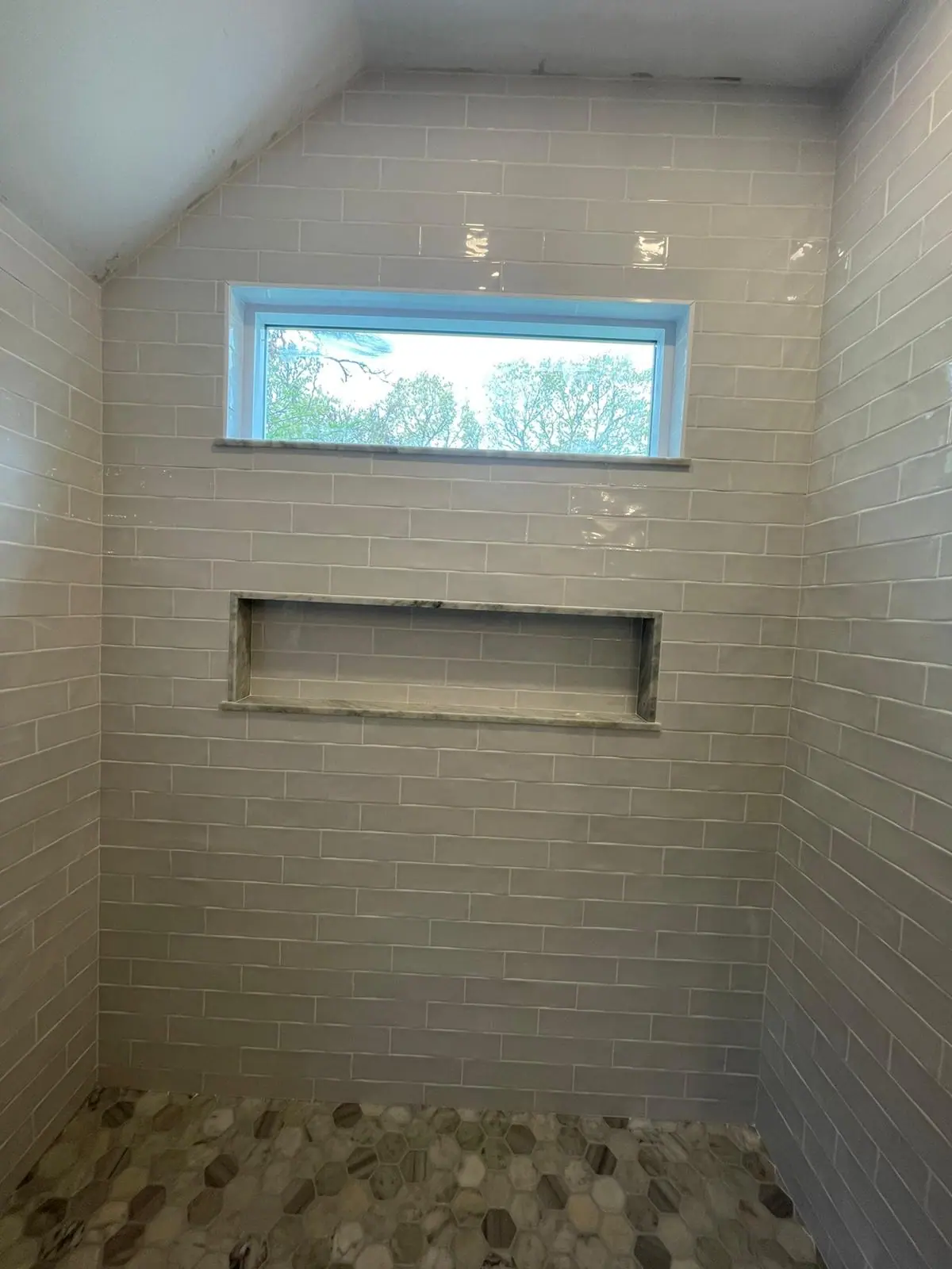 Shower with white subway tile, a window, a long recessed niche and a pebble tile floor