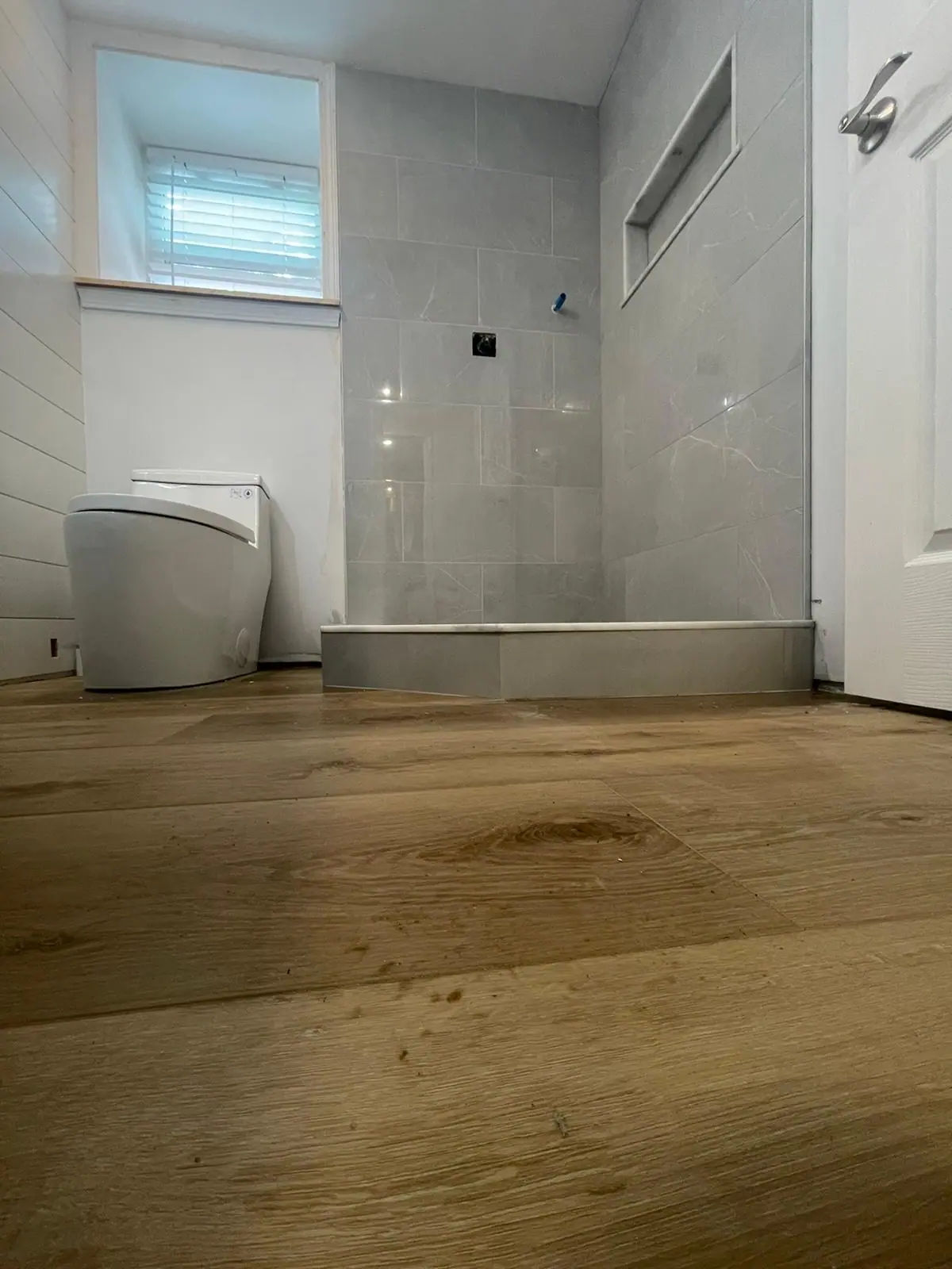 Bathroom with wood-look flooring and a gray tiled walk-in shower with a curb